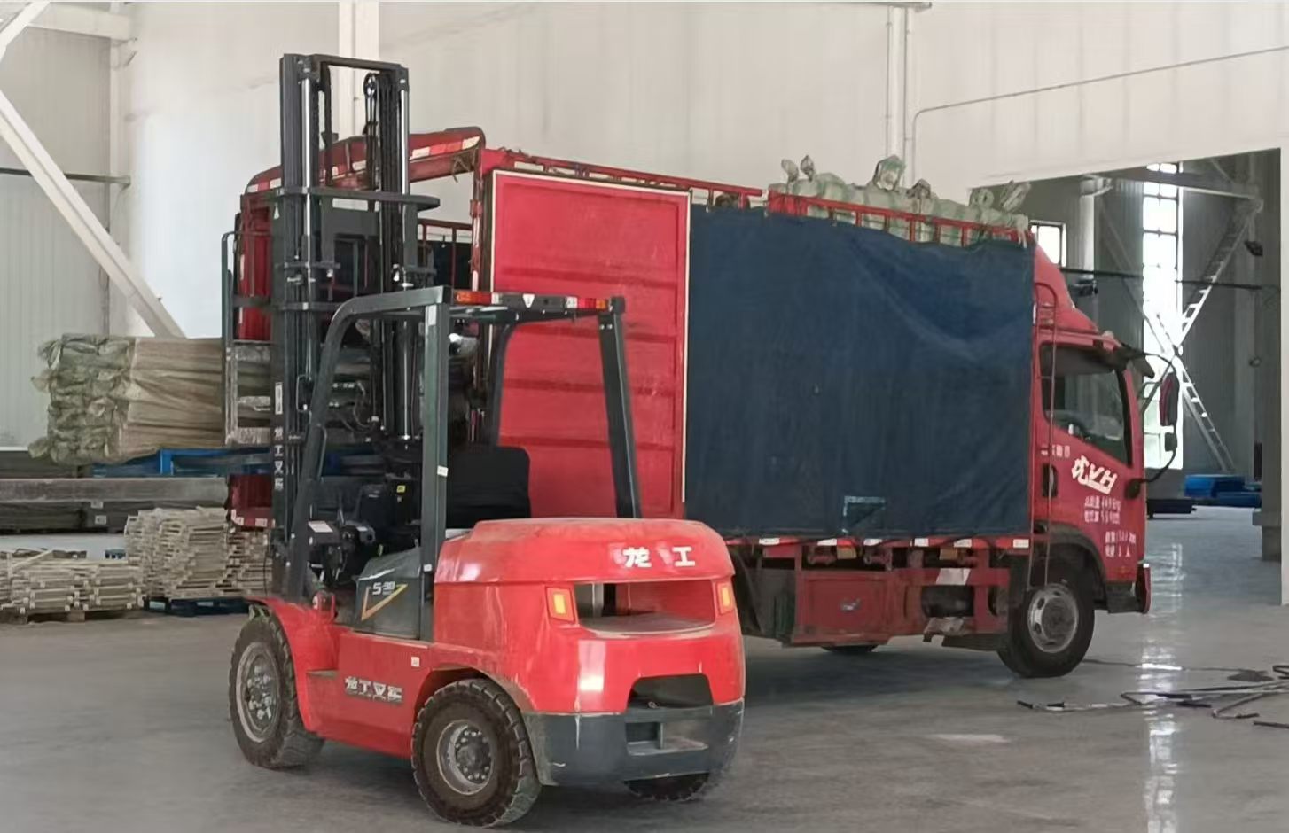 Carretilla elevadora de f&aacute;brica cargando paletas de bastones de fibra de carbono empaquetados en un cami&oacute;n de log&iacute;stica